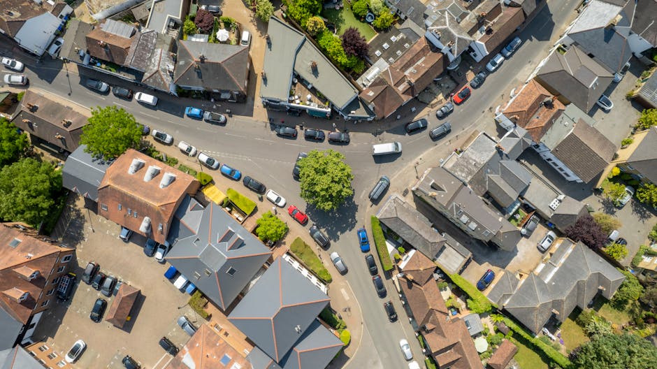 A black-and-white aerial photograph of a suburban residential area showing rows of terraced houses with pitched roofs, some covered with tiles and others with flat roofing materials. The houses are ar