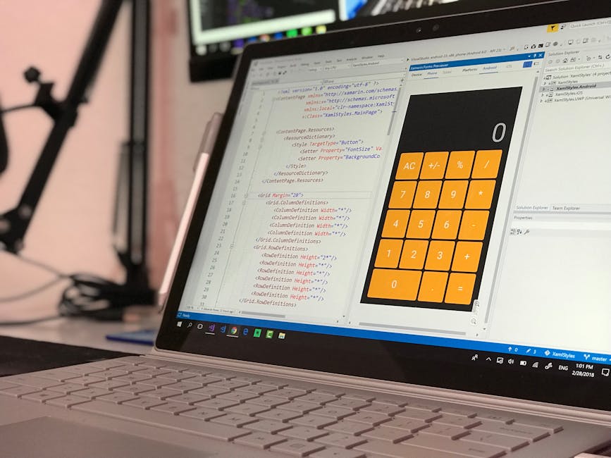 A laptop screen displaying lines of HTML code in a text editor alongside a large, orange calculator application with a white display, situated on a desk in a professional workspace. The screen feature